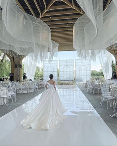 a woman in a wedding dress is walking down the runway with white tables and chairs