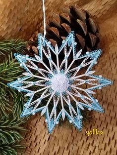 a snowflake ornament hanging from a pine cone on top of a table