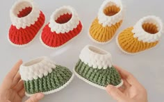 someone is holding some crocheted baby shoes in front of their hand and two pairs of slippers on the floor