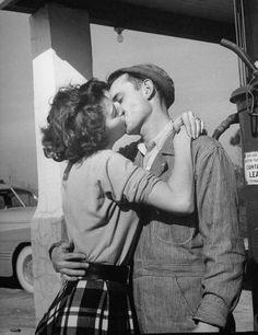 a man and woman kissing in front of a gas station