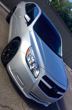 the front end of a silver car parked in a parking lot next to a building