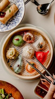 a person holding chopsticks over a bowl of food on a table with other plates and utensils