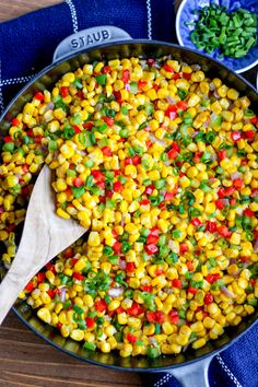 a skillet filled with corn and vegetables on top of a blue towel next to spoons