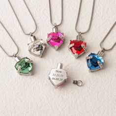 four different colored heart shaped necklaces on a white surface with the names of their loved ones