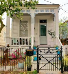 a white house with a black gate and flowers in the front yard on a sunny day