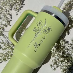 a green water bottle sitting on top of a table next to some flowers and leaves