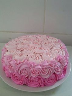 a cake with pink frosting and roses on the top is sitting on a white plate