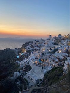 the sun is setting over some white buildings by the ocean in oia, greece