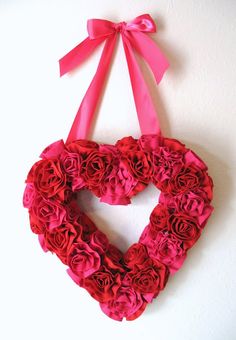 a heart shaped wreath with pink roses hanging on the wall next to a white wall