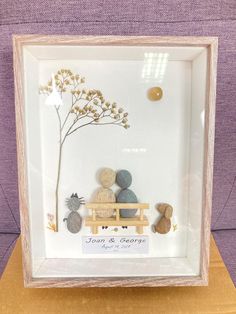 a glass frame with rocks and flowers in it