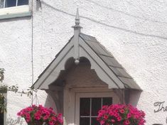 a white building with pink flowers hanging from it's windows and potted plants