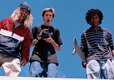 three young men standing on top of a building holding skateboards and looking at the camera