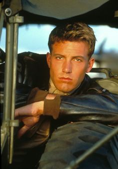 a man in a leather jacket leaning on the steering wheel of a vehicle