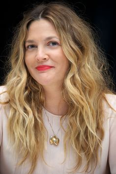 a woman with long blonde hair wearing a white shirt and red lipstick is looking at the camera