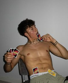 a shirtless man is holding cards in front of his face while sitting on a chair