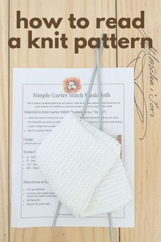 a knitted white blanket sitting on top of a piece of paper next to knitting needles