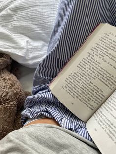 an open book laying on top of a bed next to a teddy bear