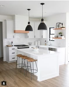 a kitchen with white cabinets and black pendant lights hanging over the island in front of two stools