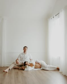 a man and woman are sitting on the floor in an empty room with white walls