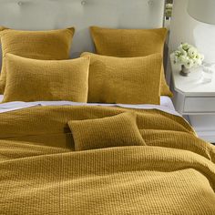 a bed with yellow sheets and pillows on top of it, next to a night stand