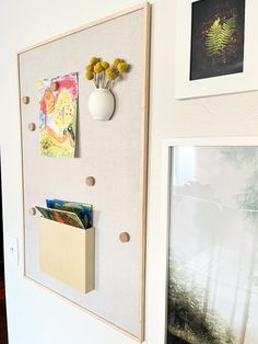 a white wall with some pictures hanging on it and a vase filled with yellow flowers