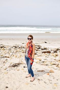 a woman standing on top of a sandy beach next to the ocean with her hands in her pockets