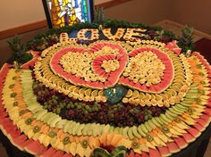 an arrangement of fruit arranged in the shape of a heart on a table with stained glass window behind it