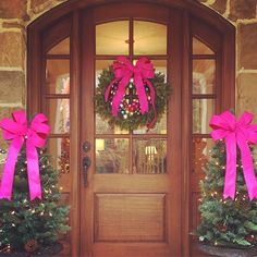 two christmas wreaths with pink bows are on the front door