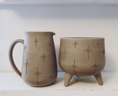 two coffee mugs sitting next to each other on a counter top in front of a white wall