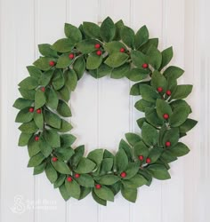 a wreath made out of green leaves and red berries hanging on a white wooden door