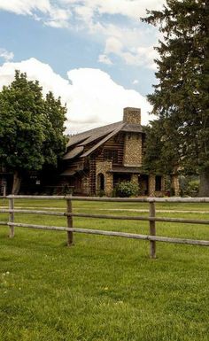 an old log cabin sits in the middle of a grassy field next to a wooden fence