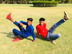 two young men sitting on the ground with their feet up in the air and one holding his leg up