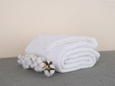 a stack of white towels sitting on top of a bed next to cotton flowers in front of a beige wall