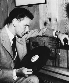 a man in a suit and tie sitting on a bench with a record player next to him