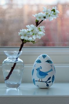 an egg sitting on a table next to a vase with flowers in it and a bird painted on it