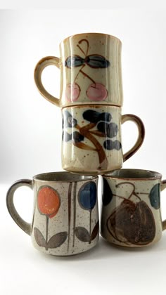 four coffee mugs are stacked on top of each other, with designs painted on them