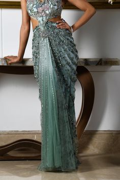 An eye-catching ensemble immersed in the marine allure of aqua blue creates an elegant look. This modern concept saree features a sleeveless blouse and a pre-draped skirt attached to each other. Botanical motifs, embroidered with fine crystals, sequins, and beads, adorn the entire ensemble, along with tulle pleats. The beauty of the wilderness perfectly interplays its role through flower motifs and deep hues, making it an exquisite piece for your nightly soirees. The sleeveless blouse features signature flower motifs embroidered with the use of crystals, beads, and sequins. Pre-draped skirt adorned with flower motifs attached to the blouse. Criss-cross pattern at the backside of the blouse. The blouse contains a metal zip at the backside. The skirt is attached to the blouse. From Moledro’s Elegant Turquoise Festive Set, Elegant Turquoise Set With Dupatta, Elegant Turquoise Wedding Sets, Blue Hand Embellished Sets For Evening, Blue Floor-length Pre-draped Saree For Wedding, Hand Embellished Blue Evening Sets, Elegant Light Blue Gown For Reception, Blue Hand Embellished Saree With Traditional Drape, Blue Hand Embellished Traditional Saree