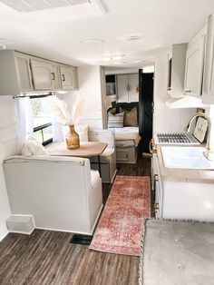 a kitchen and living room in a mobile home with wood flooring, white cabinets and appliances