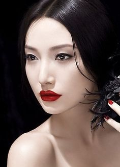 a woman with black hair and red lipstick holding a spider on her finger, wearing white gloves