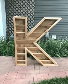 the letter k is made out of wood and sits in front of a building with grass