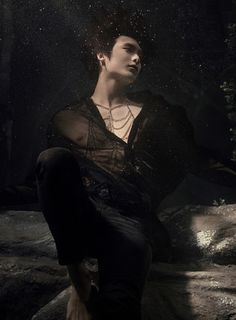 a young man sitting on top of a rock in the dark with water droplets coming from his face