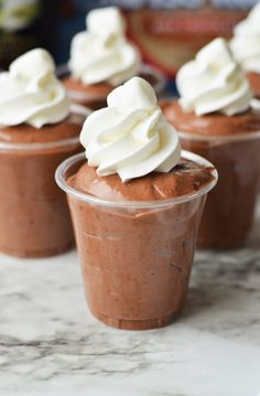 four cupcakes with whipped cream on top are sitting on a marble countertop