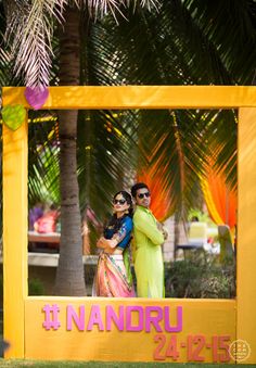 two people standing in front of a yellow frame with the words nanndru on it