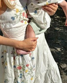 a woman holding a small child in her arms while wearing a white dress and hat