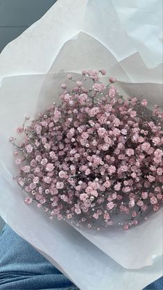 a bouquet of pink flowers sitting on top of a white paper wrapper in someone's lap