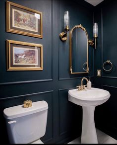 a white toilet sitting next to a sink in a bathroom under framed pictures on the wall