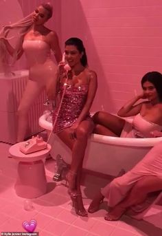 three women in pink bathing suits are sitting in a bathtub and posing for the camera