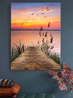 a wooden dock with birds flying over the water at sunset in front of a lake