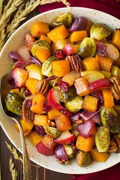 a white bowl filled with assorted veggies next to a fork and spoon