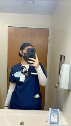 a woman in scrubs taking a selfie in front of a mirror with a camera